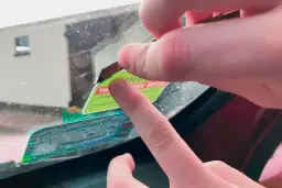 Dłonie usuwają naklejkę z szyby samochodu. Użyj żyletki, by łatwo dowiedzieć się, jak usunąć naklejkę z szyby samochodu.