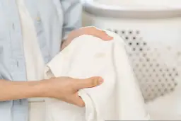 Dłonie trzymają białą bluzkę z plamami podkładu.