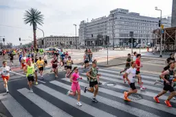 Uczestnicy biegu na ulicach Warszawy, biegacze przekraczają pasy. Biegi Polska to emocje i sport.
