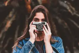 Młoda kobieta z aparatem Olympus Trip 35, gotowa do zrobienia zdjęcia. Wzór umowy z fotografem czeka na podpis.
