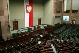 Sala plenarna Sejmu RP z godłem Polski i rzędami zielonych foteli.