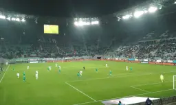Mecz Ekstraklasy na żywo! Piłkarze w zielonych i białych strojach grają na zielonej murawie stadionu. Gdzie oglądać Ekstraklasę? Na tym stadionie!