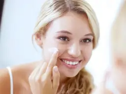 Uśmiechnięta blondynka aplikuje krem na policzek, sprawdzając, czy krem Nivea dobrze nawilża.