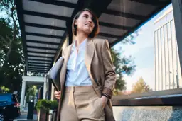 Kobieta w eleganckim stroju, symbolizującym power dressing, trzyma laptopa, gotowa na kolejne wyzwania biznesowe.