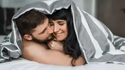 Para, przytuleni pod kołdrą, czule całujący się. Idealna randka do łóżka.