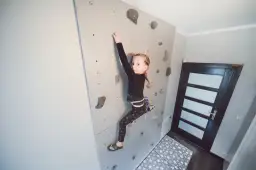 Dziewczynka wspina się po domowej ściance wspinaczkowej. To świetny sposób, by pokazać, jak zrobić ściankę wspinaczkową dla dzieci.