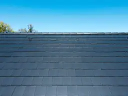 Ciemnoszara dachówka płaska ułożona na mijankę, tworząca równą, nowoczesną powierzchnię dachu pod błękitnym niebem.