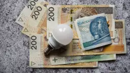 Biała żarówka LED leży na stosie polskich banknotów o nominałach 200 i 50 złotych.