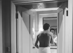 Mężczyzna w ręczniku patrzy w lustro, zastanawiając się, czy częste golenie zwiększa zarost.