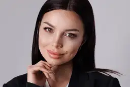 Elegancka kobieta w czarnej marynarce, opierająca podbródek na dłoni, pozuje w studiu.