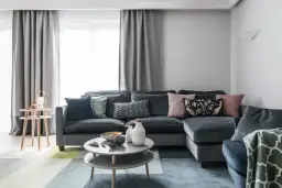 Szara kanapa z kolorowymi poduszkami i geometrycznym dywanem.