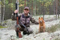Myśliwy w kamuflażu z psem i strzelbą w lesie. Czy myśliwy może sam polować? Z pewnością, zwłaszcza z takim pomocnikiem.