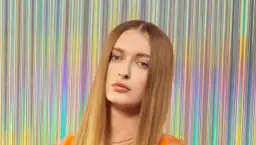 Sophie, top model o długich, blond włosach, pozuje na tle błyszczącej, tęczowej kurtyny.