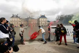 Protestujący z racami i dmuchanym obiektem przed budynkiem w Paryżu.