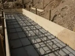 Siatka zbrojeniowa w deskowaniu fundamentu. Widać regularny układ, co ile strzemiona na fundament, gotowe do zalania betonem.