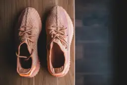 Pomarańczowe sneakersy z plecionki, idealne na szeroką stopę, leżą na drewnianym blacie.
