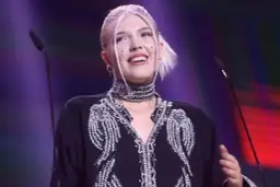 Daria Zawiałow w błyszczącej kreacji, z błyszczącymi ozdobami na twarzy, uśmiecha się na scenie.