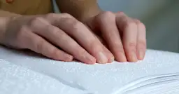 Dłonie osoby czytającej książkę w alfabecie Braille'a.