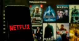 Telefon z logo Netflix na tle ekranu z filmami. Zastanawiasz się, co obejrzeć na Netflixie?