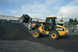 Żółta ładowarka JCB 406 z podniesioną łyżką, gotowa do pracy. Dane techniczne tej maszyny pozwalają na efektywne przenoszenie materiałów.