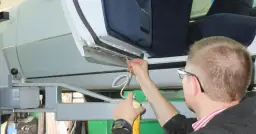 Mężczyzna aplikuje środek do zabezpieczenia śrub przed korozją na progu samochodu.