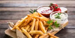 Chrupiące frytki z ketchupem i majonezem na drewnianym tle.