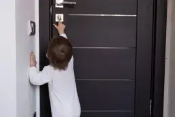 Dziecko próbuje dowiedzieć się, jak zablokować drzwi od wewnątrz, naciskając przycisk na zamku.