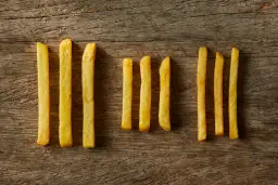 Złociste frytki Aviko ułożone rzędami na drewnianym tle.