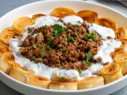 Danie z mielonej wołowiny, jogurtu i roladek z ciasta filo, posypane natką pietruszki.