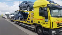 Żółta laweta z autami, w tym Volkswagenem i Skodą. Zastanawiasz się, ile kosztuje sprowadzenie auta z Holandii?