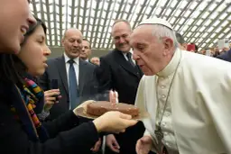Papież Franciszek zdmuchuje świeczki na torcie urodzinowym, trzymanym przez kobietę.