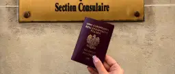 Polski paszport w dłoni przed tabliczką "Section Consulaire". Czy do Francji trzeba paszport? Tak, jeśli nie jesteś obywatelem UE.