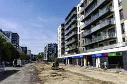 Budowa osiedla mieszkaniowego z widocznymi sklepami na parterze i placem budowy.