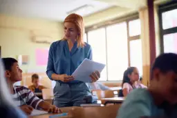 Nauczycielka z dokumentami w ręku wyjaśnia uczniom, co to znaczy nauczyciel mianowany. W klasie panuje skupienie.
