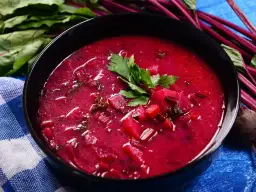 Miseczka zupy z botwiny z kawałkami buraków i natką pietruszki, obok łodygi botwiny.