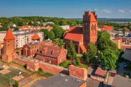 Zamek krzyżacki w Lęborku, z charakterystyczną wieżą i ceglaną architekturą, otoczony zielenią i miejską zabudową.