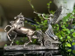 Figurka Nike, bogini zwycięstwa, w rydwanie zaprzężonym w dwa konie, na tle zieleni.