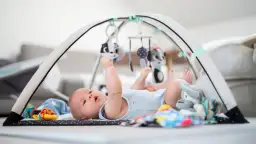 Niemowlę leży na macie sensorycznej pod łukiem z zabawkami.