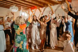 Ludzie tańczą na weselu, podnosząc ręce w górę. Wszyscy świetnie się bawią, jak zem lecioł na wesele.