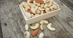 Drewniana skrzynka z orzechami: migdały, pistacje i orzechy nerkowca na drewnianym tle.