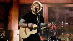 Ed Sheeran spielt Gitarre und singt auf einer Bühne.