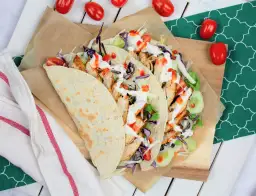 Kebab w tortilli z kurczakiem, warzywami i sosami, obok pomidorki.