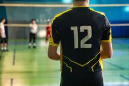 Męski strój siatkarski z numerem 12 na plecach. Zawodnik gotowy do gry na boisku.