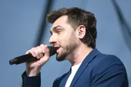 Kamil Bednarek śpiewa do mikrofonu w granatowej marynarce.