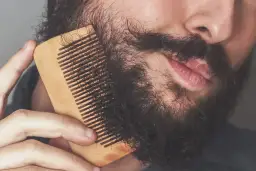 Mężczyzna czesze brodę drewnianym grzebieniem, szukając sposobu, jak zmiękczyć zarost.