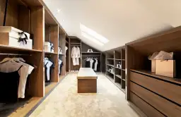 Nowoczesna garderoba ze skosem, z drewnianymi frontami, jasnym dywanem i ławką. Idealne miejsce na przechowywanie ubrań.