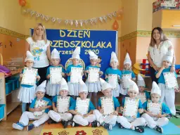 Dzieci w strojach smerfów z dyplomami, z nauczycielkami w tle.