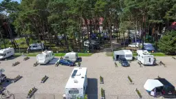 Kampery i przyczepy kempingowe na żwirowym polu namiotowym w lesie sosnowym. Widok z lotu ptaka na sea camp Rogowo.