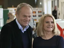 Donald Tusk z żoną, uśmiechnięci, w tle wyborcze plakaty.
