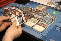 Ręce trzymają karty z gry kolekcjonerskiej. Na stole leżą karty z Pokémonami, m.in. Ditto i Hoothoot.